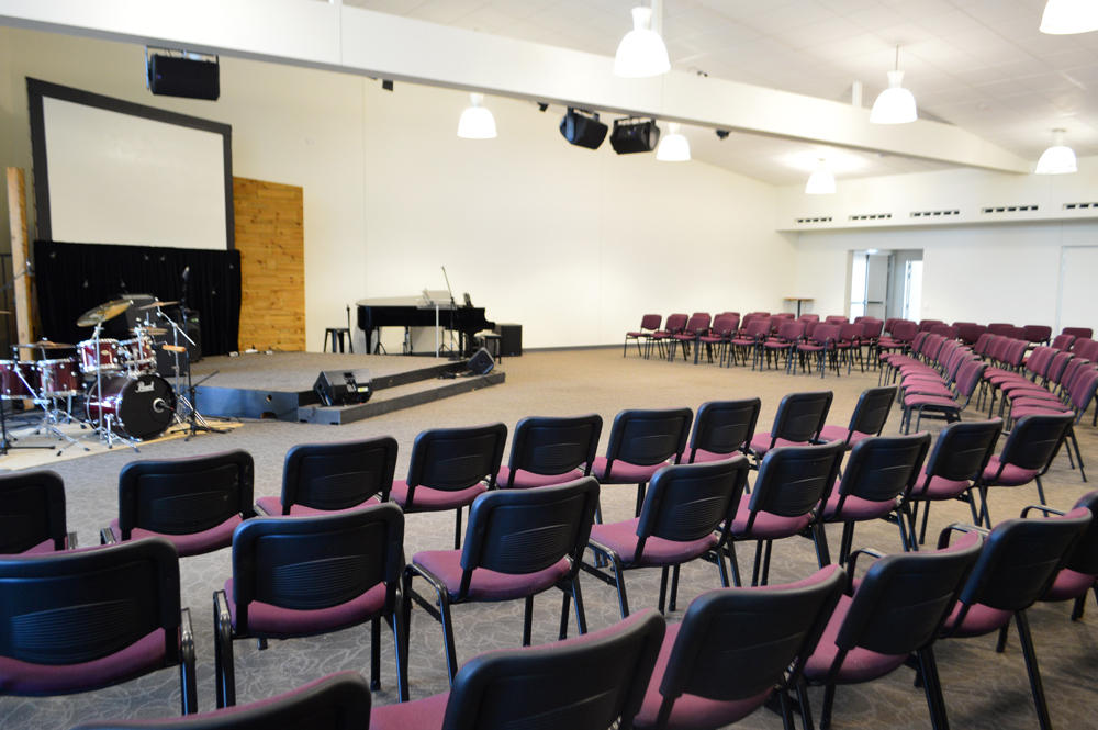 The large auditorium of the church is filled with chairs lined up in rows. At the front of the room there is a stage with musical instruments including a piano, drum kit and guitars.