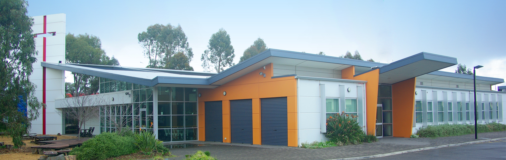 The church building stands tall and proud as the large cross on the front of the building reaches out towards the sky. The church is surrounded by trees and shrubs in a native garden.