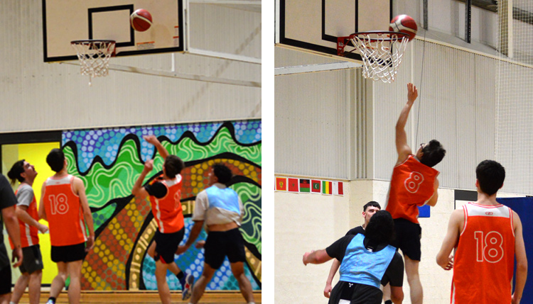 Two basketball teams playing against each other watch as a player jumps high into the air launching the ball towards the goal.