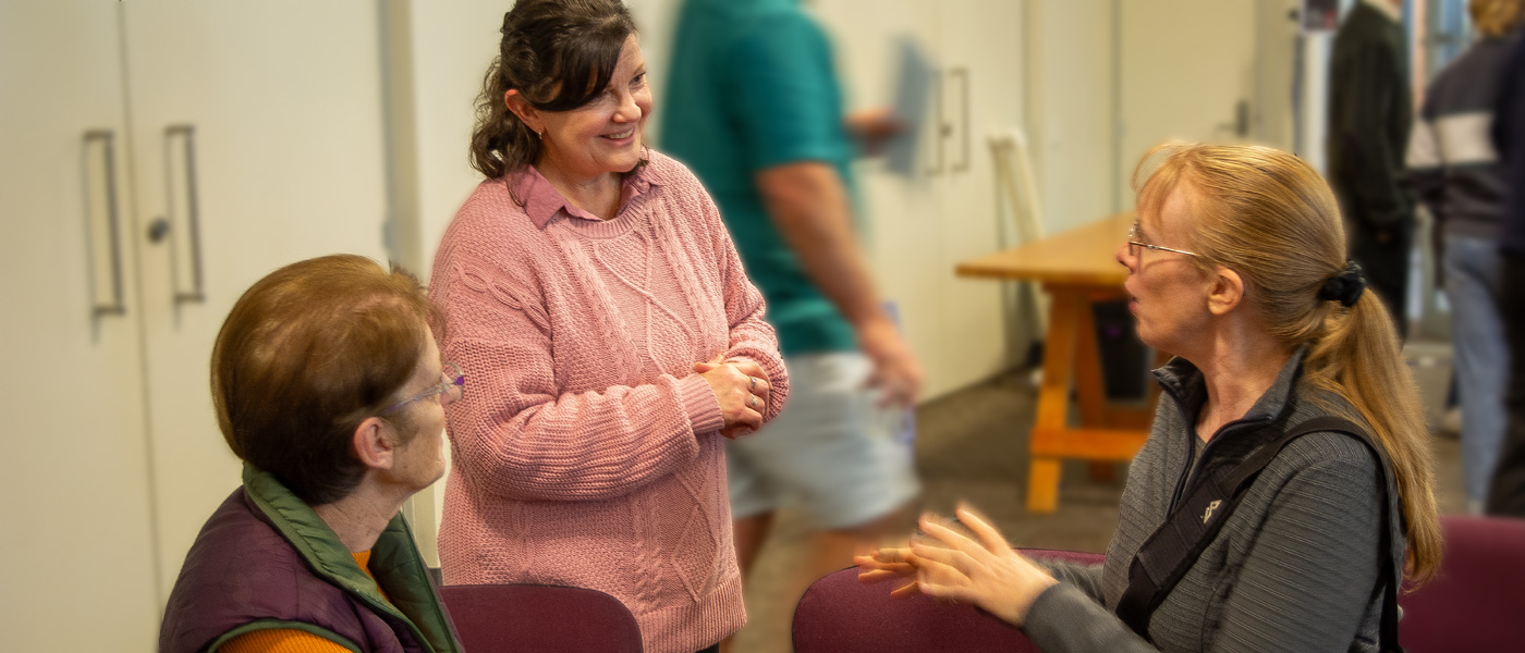A group of three women gathered together having a friendly conversation, smiling and laughing with each other.