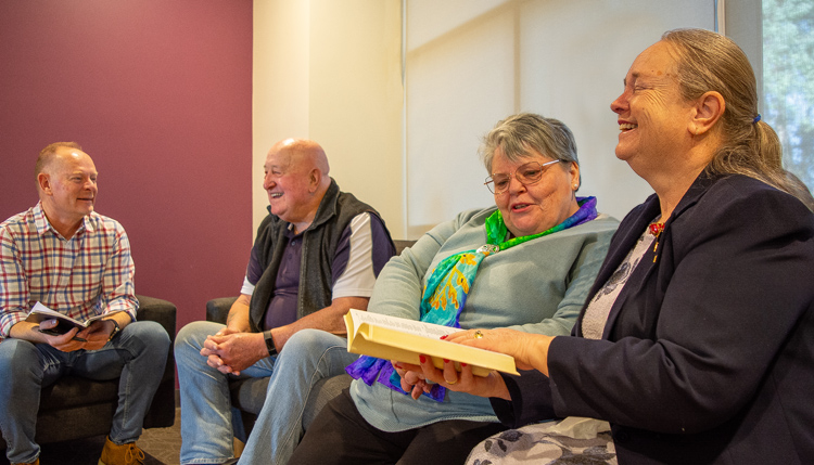 A group of adults sitting on couches together, open bibles in hand, smiling and engaged in deep conversation together. 