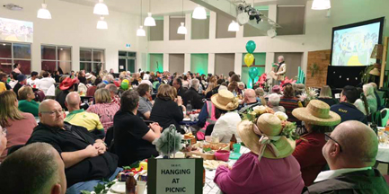 The church building is filled with people sitting in groups around tables filled with decorations, eagerly awaiting quiz questions to be read.