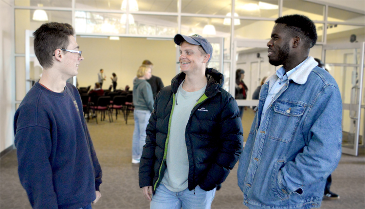 Three young men stand together, engaged in conversation smiling at each other.